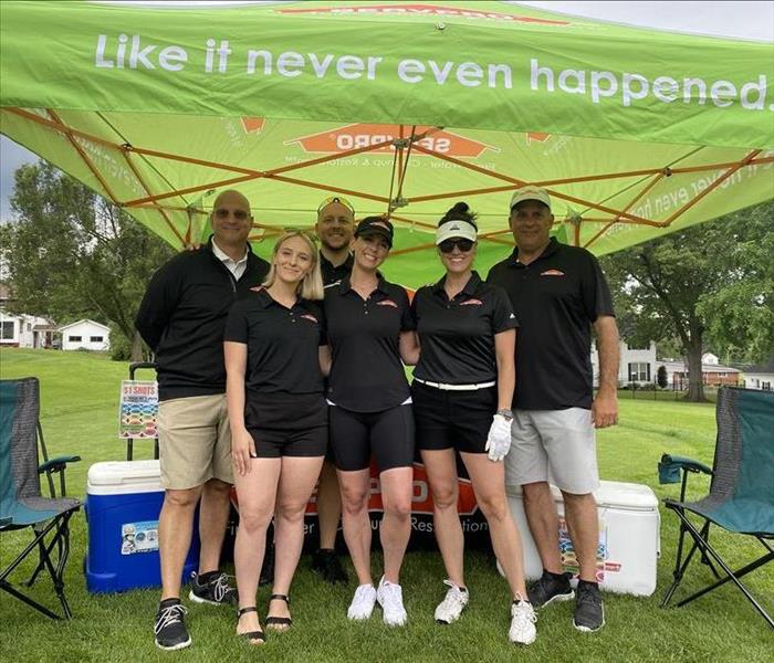 SERVPRO team members stand under a tent at a golf outing.